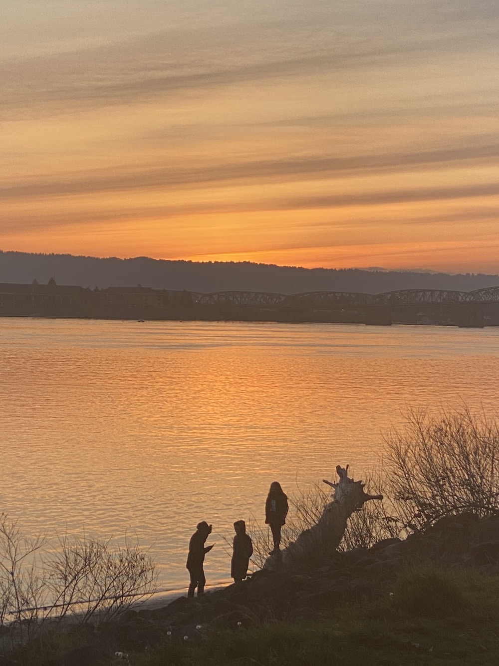 three people on shoreline at sunset